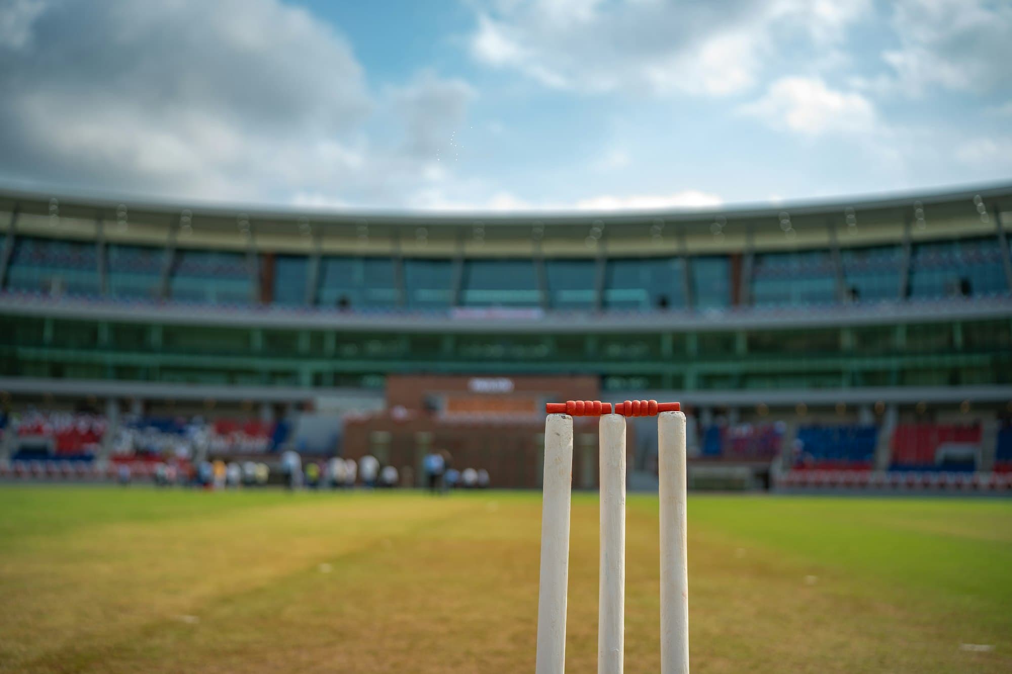 Cricket stumps on the pitch in front of a stadium pavilion